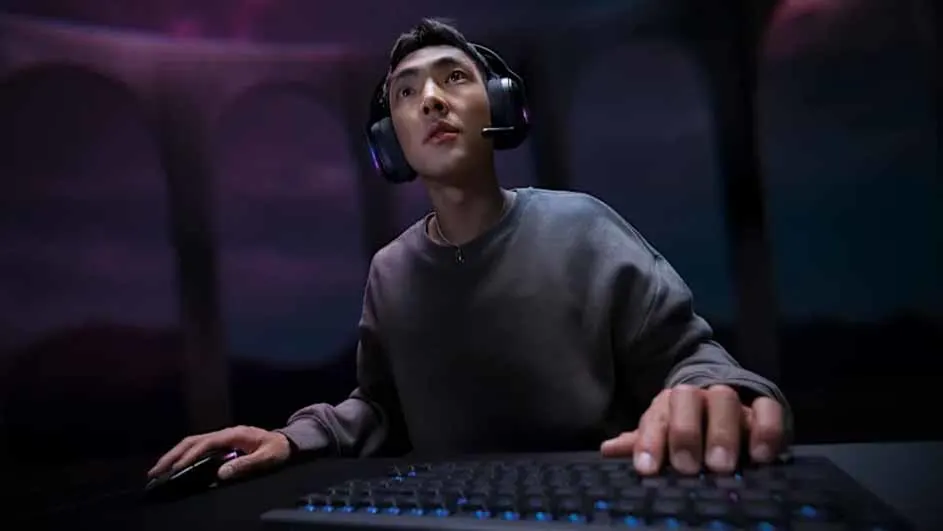 Man geconcentreerd tijdens het gamen, met een Logitech G-headset en een toetsenbord en muis in een donkere kamer met paarse verlichting.