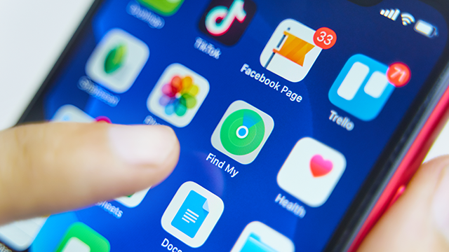Een vinger tikt op een blauw smartphonescherm met app-pictogrammen, waaronder TikTok, Facebook, Trello en Find My.
