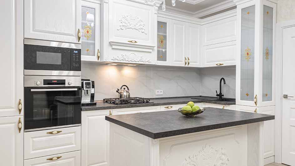 Witte keuken met apparatuur, kookplaat, gootsteen en aanrecht. Een schaal met groene appels staat op het aanrecht.