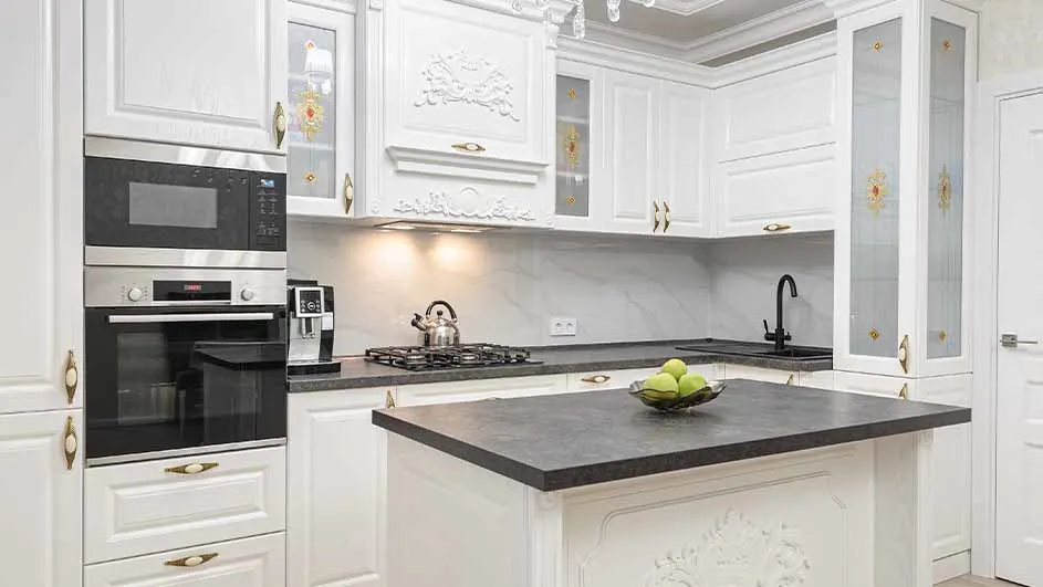 Witte keuken met apparatuur, kookplaat, gootsteen en aanrecht. Een schaal met groene appels staat op het aanrecht.