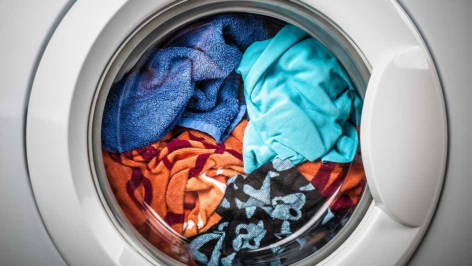 A white washing machine with a round glass door filled with mixed color clothes, including blue, orange, and black.