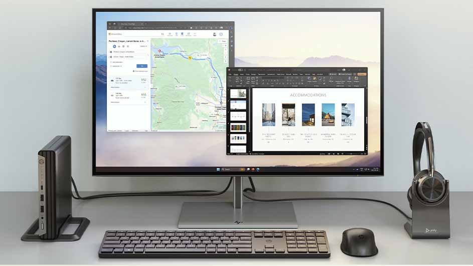 Een bureau met een monitor waarop een kaart en een presentatie te zien zijn, een toetsenbord, een muis, een computer en een hoofdtelefoon.