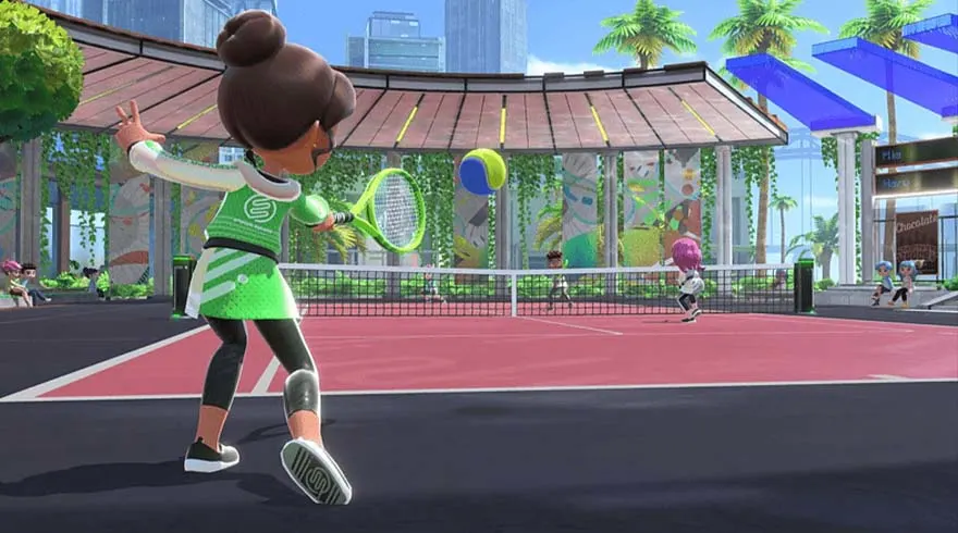 Een tennisspeler in groene sportkleding slaat een bal op een roze tennisbaan met een net en gebouwen op de achtergrond.
