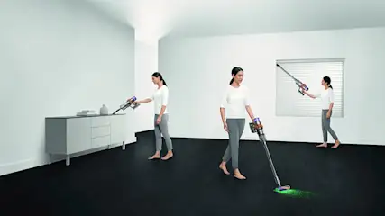Een vrouw stofzuigt een kamer met een draadloze stofzuiger, tegen een witte achtergrond.