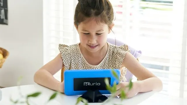 Meisje zit aan een witte tafel en kijkt naar een blauwe Kurio-tablet. Er staat een plant op de voorgrond en een raam op de achtergrond.