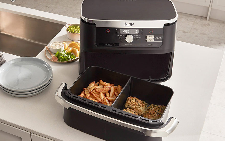 Black Ninja air fryer with dual drawers on white worktop. Chips on left, roasted meat on right. Digital display shows 240°C and 10 minutes.