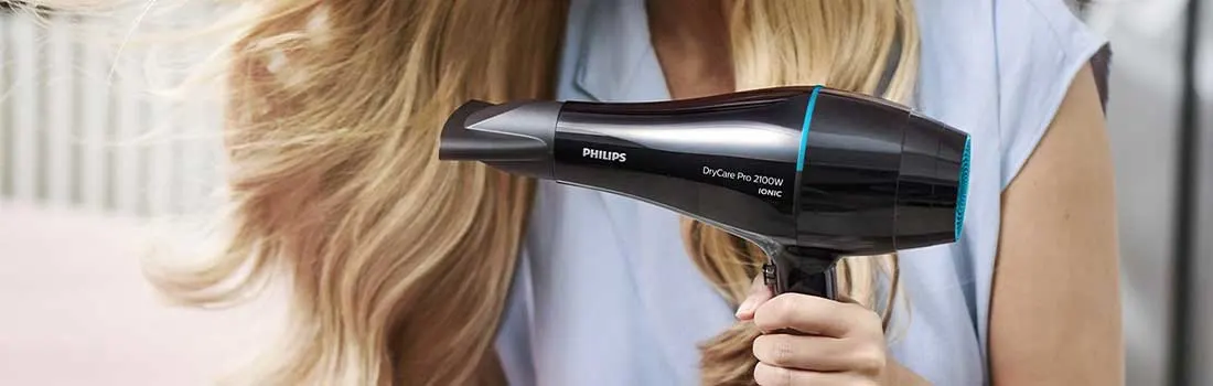 Vrouw met lang blond haar föhnt haar lokken met een zwarte Philips haardroger; haar glanzende haar waait soepel langs haar schouders.