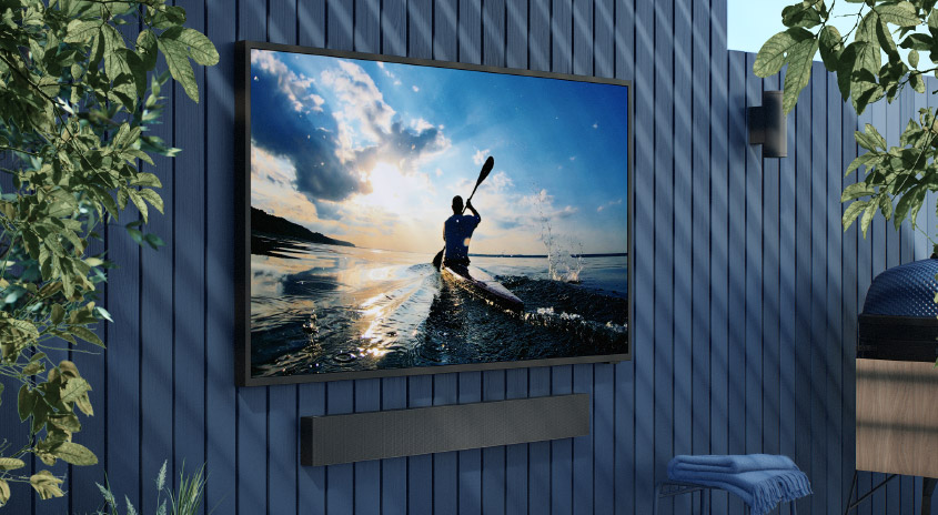 Ein Fernseher, der an einer blauen Holzwand montiert ist, zeigt ein Paddelbild. Ein Lautsprecher befindet sich unter dem Fernseher.