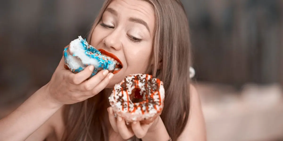 Eine Frau beißt in einen Doughnut während sie einen zweiten hält und ansieht.