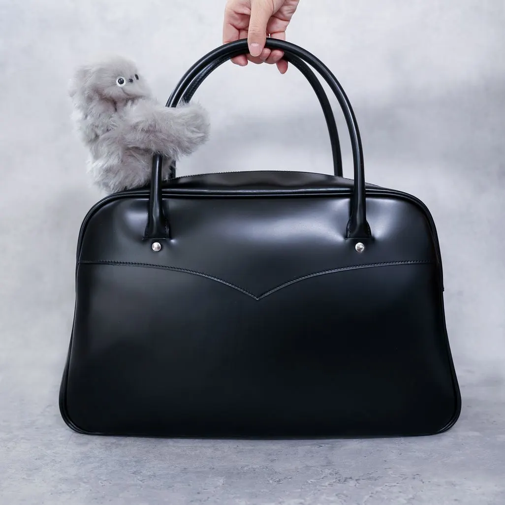 Hand haelt schwarze Tasche mit kleinem Plueschtier das am Henkel haengt