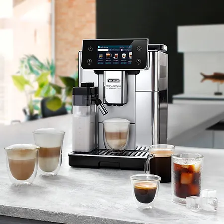 Eine silberne Kaffeemaschine steht auf einer Theke, umgeben von verschiedenen Kaffeesorten in Gläsern, darunter ein Espresso und ein Eiskaffee.