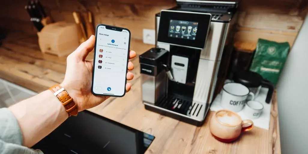 DeLonghi PrimaDonnaSoul im Hintergrund davor eine Hand die ein Smartphone hält