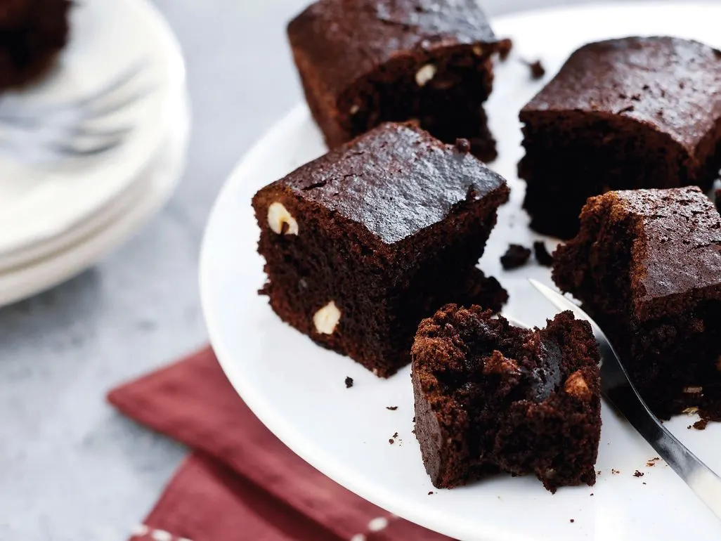 Mehrere Stücke saftiger Schokoladenbrownie mit Nussstücken auf einem weißen Teller.