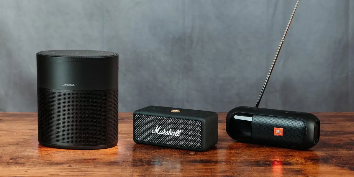 Drei Lautsprecher von Bose, Marshall und JBL stehen nebeneinander auf einem Holztisch.