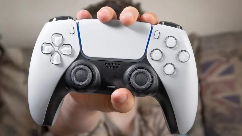 Eine Hand hält einen weißen und schwarzen PlayStation 5 DualSense Controller mit transparenten Tasten und blauer Beleuchtung.