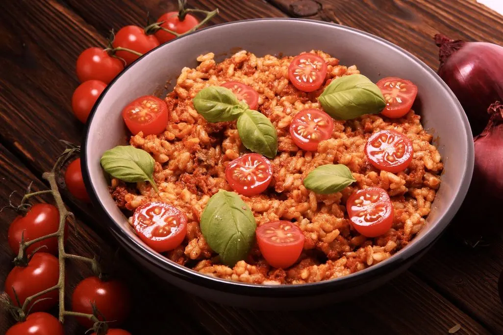 Reisgericht mit Tomatensauce halbierten Cherrytomaten und Basilikumblättern.