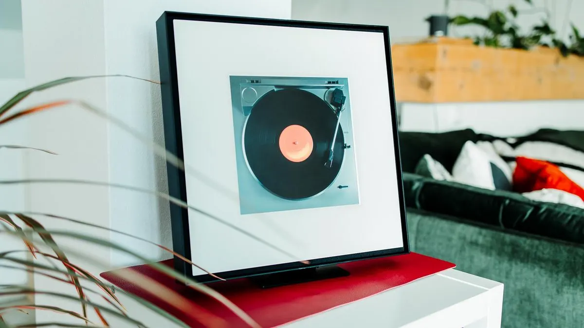 Samsung Music Frame auf roter Unterlage. Sofa und Pflanzen im Hintergrund.