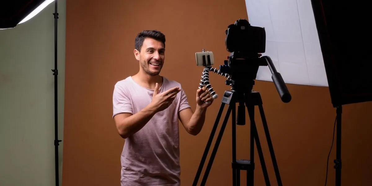 Mann steht vor einer Kamera und hält ein Stativ mit Smartphone in der Hand in einem Fotostudio