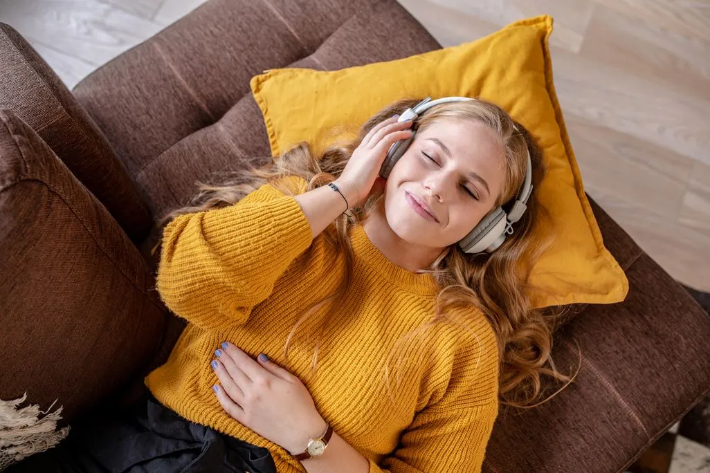 Eine Frau liegt entspannt auf dem Sofa, trägt Over-Ear-Kopfhörer und berührt sie.