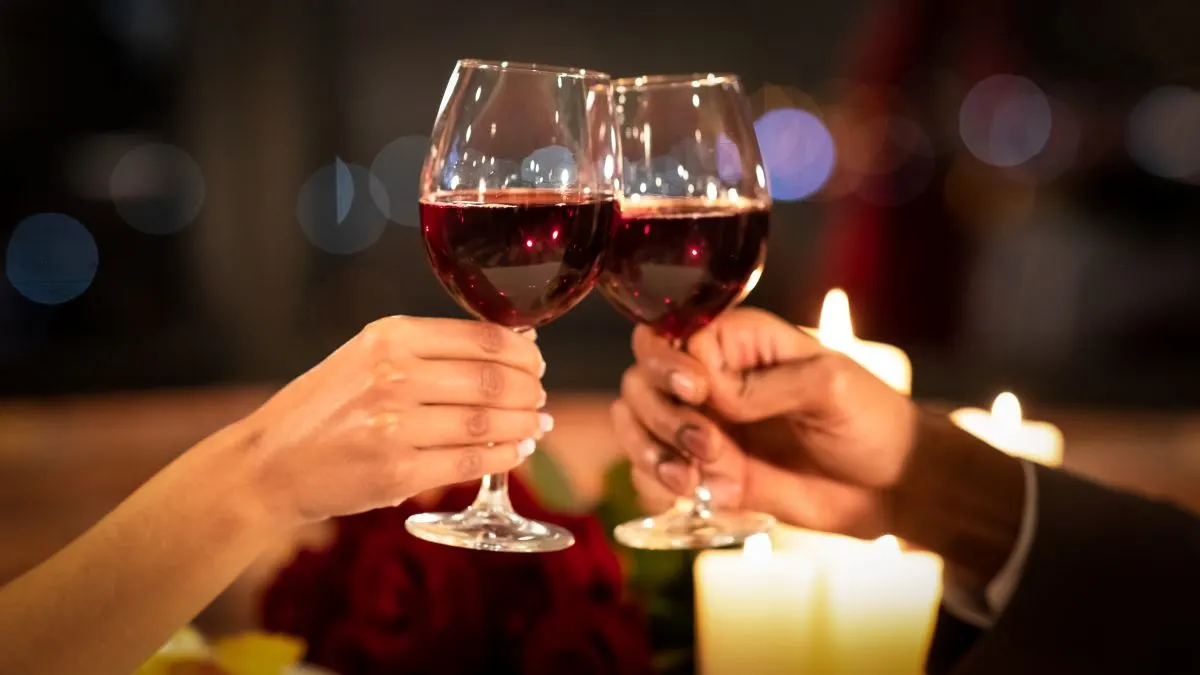 Zwei Hände mit Weingläsern die sich zu Prosten. In den Weingläsern befindet sich Rotwein.