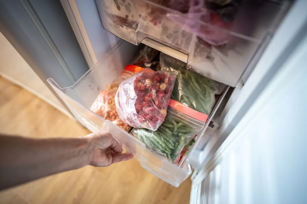 Eine Männerhand öffnet eine Schublade voller gefrorenem Obst und Gemüse von einem Gefrierschrank