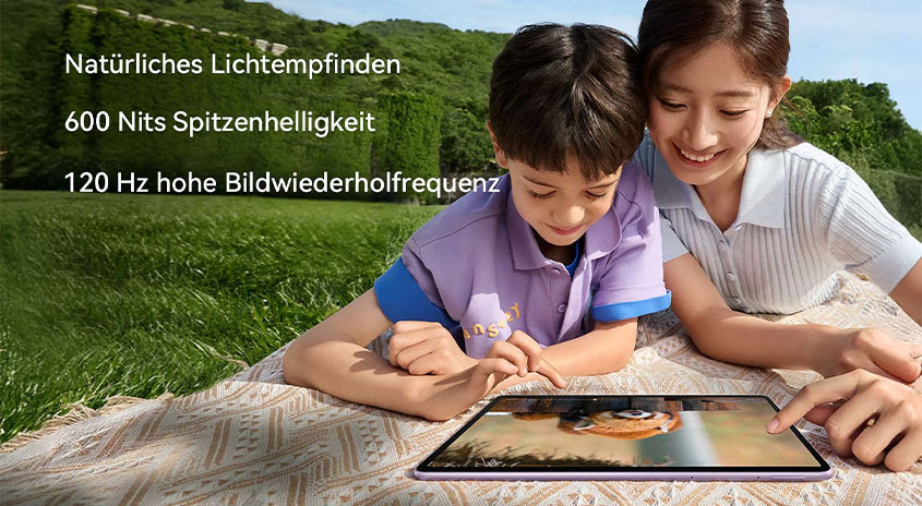  Erwachsene und Kind liegen auf einer Wiese und schauen gemeinsam auf ein Tablet; links im Bild Texte zu natürlichem Lichtempfinden, 600 Nits und 120‑Hz-Bildrate.