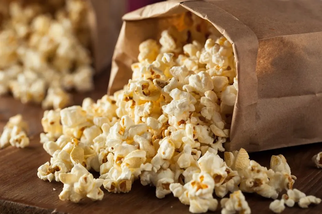 Frisch zubereitetes Popcorn quillt aus einer Papiertüte auf einen Holztisch.