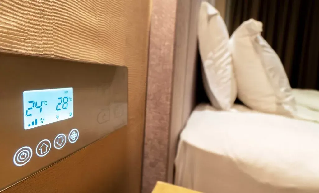 Digitales Thermostat zeigt Temperatur an, daneben ein Bett.