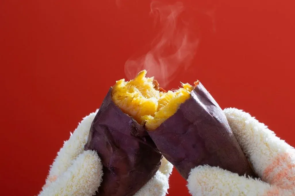 Im Herd gegrillte Süßkartoffel wird von zwei Händen aufgebrochen.