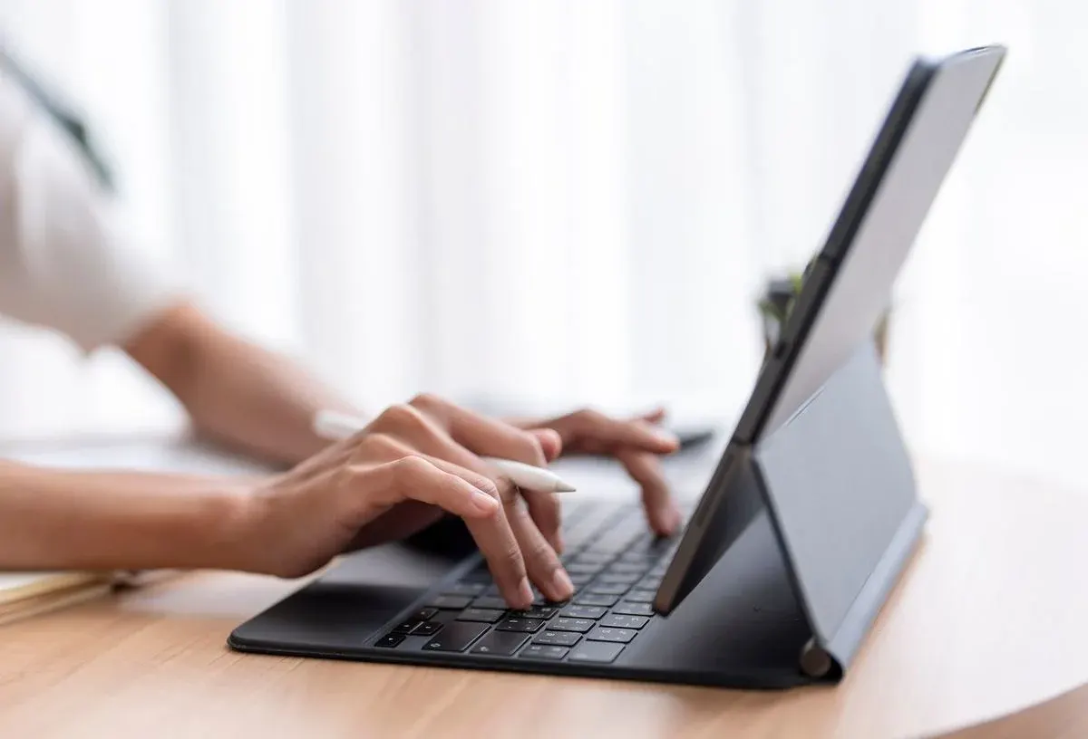 Hände tippen auf einer Tastatur, die an ein Tablet gedockt ist.