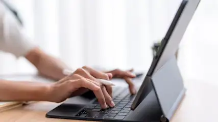 Hände tippen auf einer Tastatur, die an ein Tablet gedockt ist.