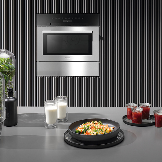 Einbauofen an einer gestreiften Wand, Tisch mit Speisen und Getränken im Vordergrund. Gläser enthalten Milch und Saft.