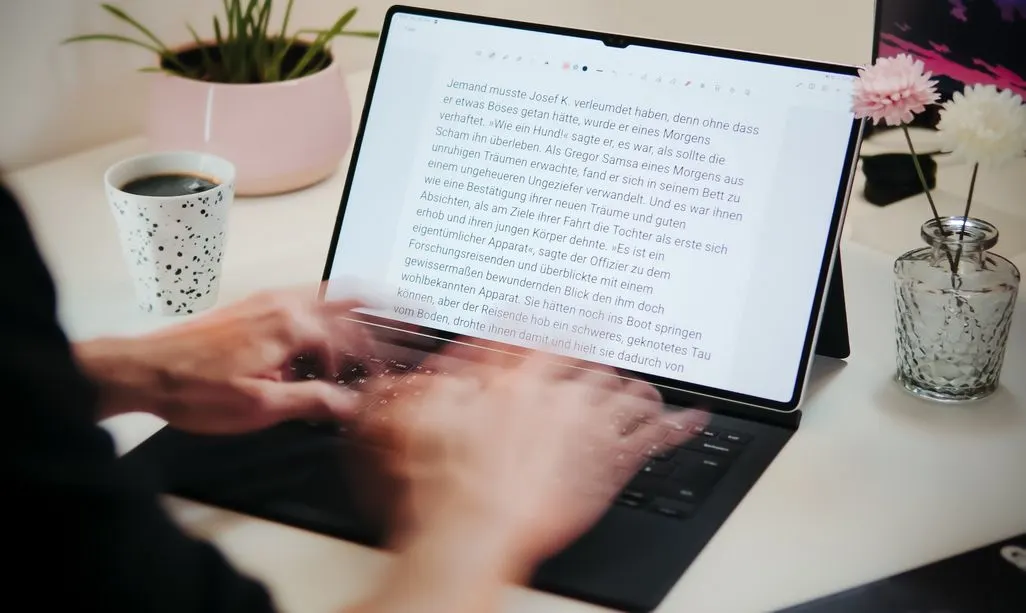Haende tippen auf Laptop-Tastatur mit deutschem Text auf Bildschirm