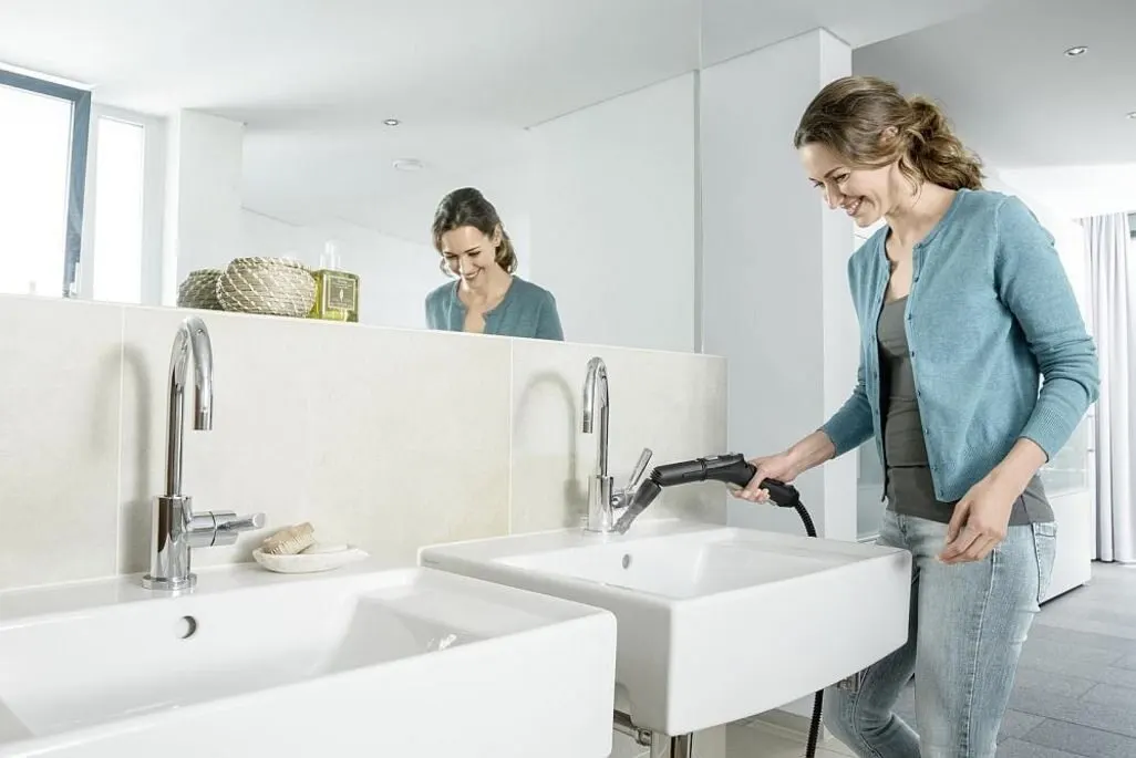 Person reinigt den Wasserhahn eines Waschbeckens mit einem Dampfreiniger