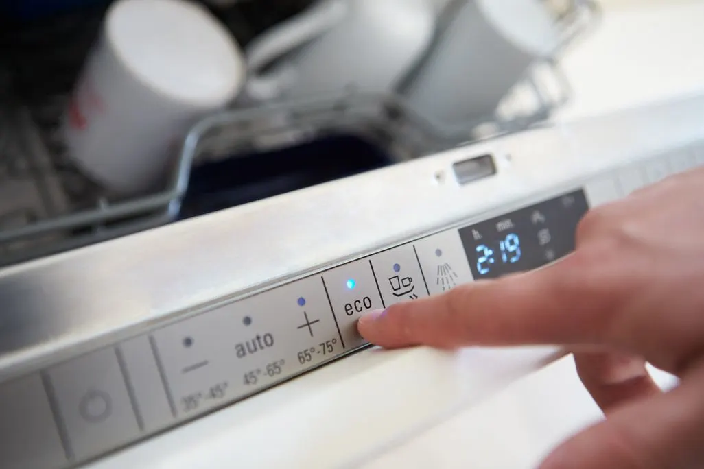 Finger drueckt die Eco-Taste an einem Geschirrspueler