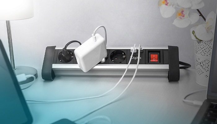 Eine praktische Digitus Steckdosenleiste im Aluminium-Design steht auf einem Schreibtisch. Neben einem beleuchteten roten Kippschalter sind ein großes weißes Netzteil, ein schwarzes Stromkabel und zwei weiße USB-Kabel eingesteckt, um Laptops und andere Geräte am Arbeitsplatz mit Strom zu versorgen.