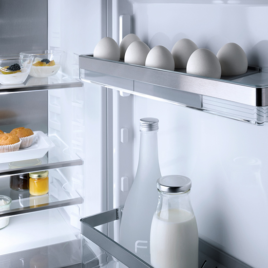 Ein Kühlschrank mit Lebensmitteln: Eier, Milchflaschen, Marmeladengläser und Desserts auf mehreren Regalen.