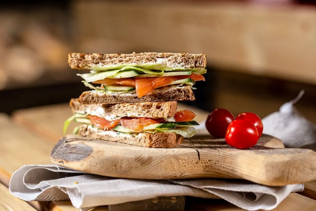 Doppelt belegtes Vollkornsandwich mit Lachs Gurke und Salat auf Holzbrett