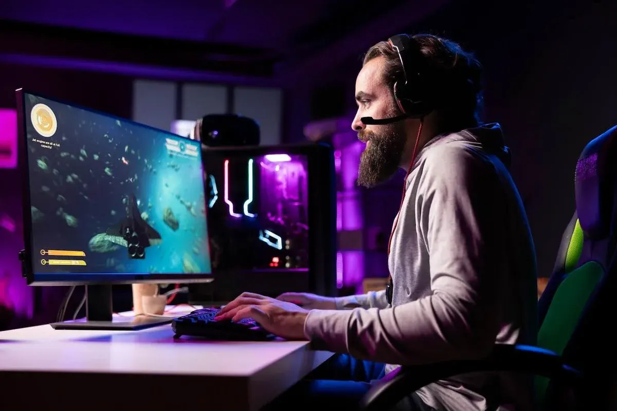 Mann mit Headset sitzt an einem RGB-beleuchteten Gaming-PC und spielt konzentriert ein Weltraumspiel auf großem Monitor in abgedunkeltem Zimmer.