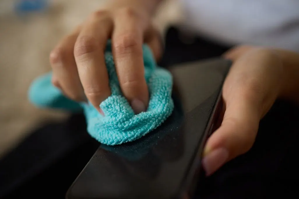 Eine Hand reinigt ein Smartphone mit einem blauen Mikrofasertuch.