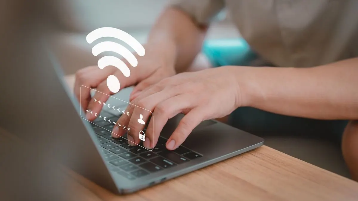 Hände tippen auf dunkler Laptop-Tastatur auf Holztisch. Weißes WLAN-Symbol und Passwortfeld mit Sternen, Benutzer- und Schloss-Symbolen.