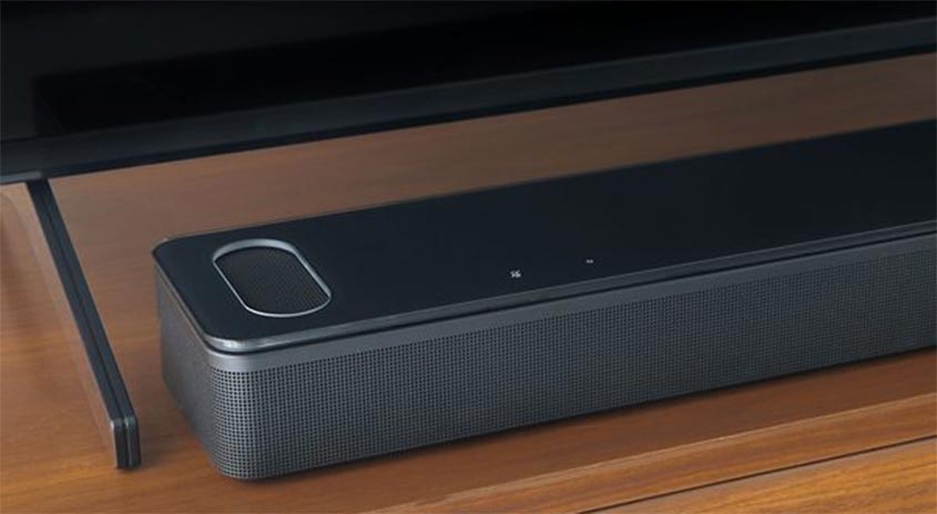 Schwarze Soundbar unter einem Fernseher auf einem Holztisch. Die Soundbar hat ein längliches Design mit einem ovalen Knopf.