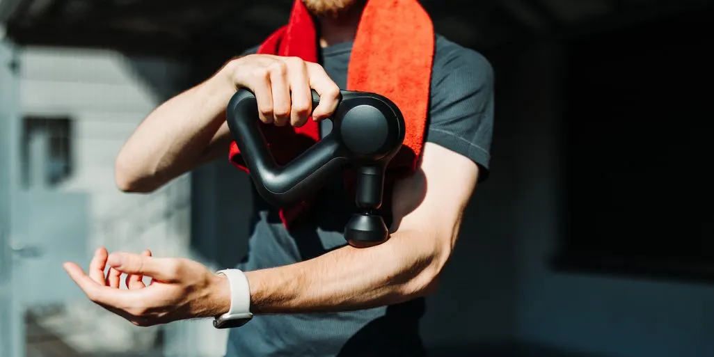 Ein Mann mit Handtuch um den Nacken massiert seinen Unterarm mit einer Massagepistole