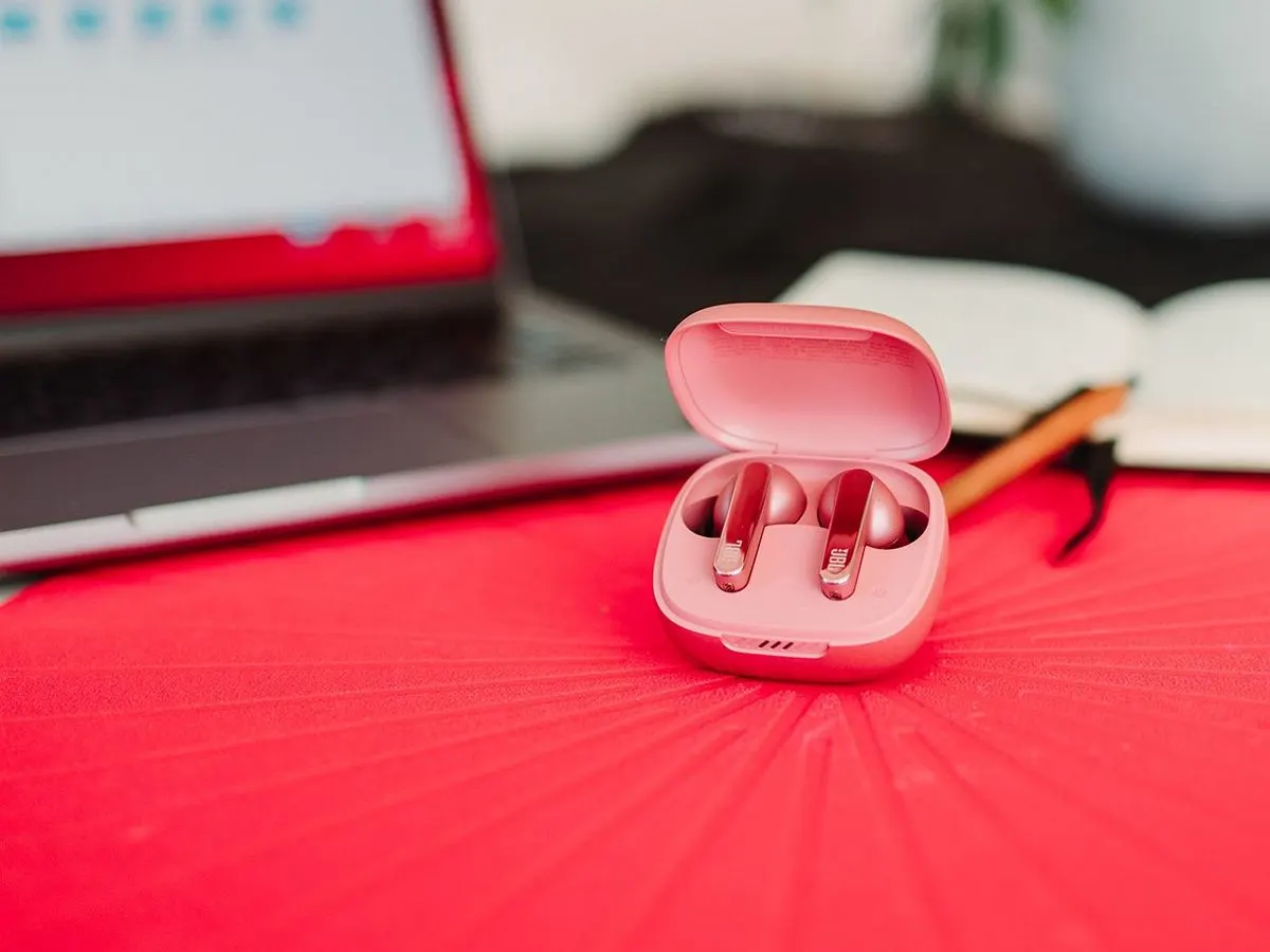 Ein offenes Ladecase mit pinkfarbenen JBL In-Ear-Kopfhörern steht auf einem roten Tisch.