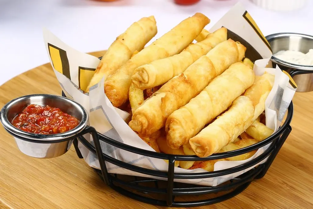 Ein Korb mit knusprigen Börek und zwei Dips in kleinen Schalen.