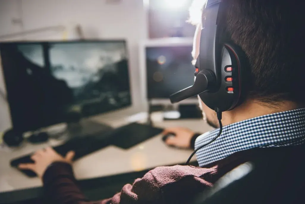 Gamer mit Gaming-Headset spielt mit Maus und Keyboard vor einem Bildschirm.