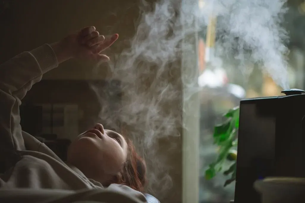 Person liegt entspannt im Zimmer und betrachtet den aufsteigenden Wasserdampf eines Luftbefeuchters.