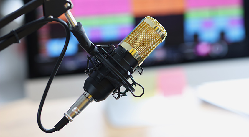 Ein goldenes Mikrofon mit schwarzer Halterung steht vor einem verschwommenen Bildschirm.