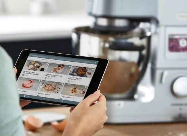 Tablet auf dem die Kenwood World App geöffnet wird um ein Rezept für den Cooking Chef XL im Hintergrund auszusuchen.