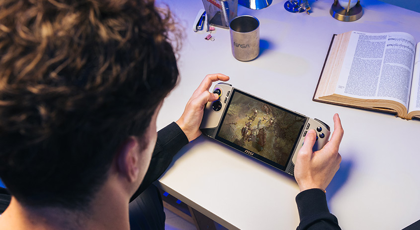 Ein tragbarer MSI-Gaming-PC wird auf einem weißen Tisch mit einem geöffneten Buch und einem Becher verwendet.